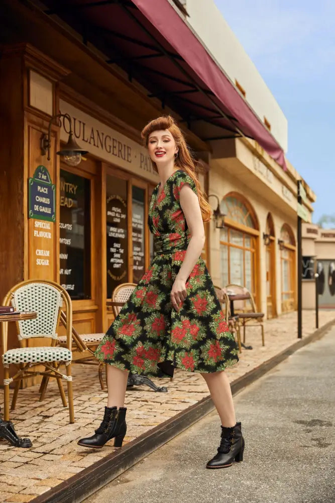 A woman wears a green floral print cotton midi dress with red and yellow blossoms featuring pockets and a fitted bodice