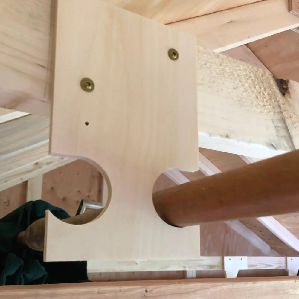 Light-colored wooden heavy duty wall mounted pole saw and pool skimmer hook bracket with two brass screws and curved cutout