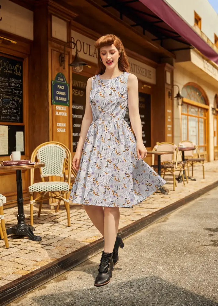 A woman wears a Pollinators vintage blue floral cotton sleeveless a-line dress with fitted waist and pockets