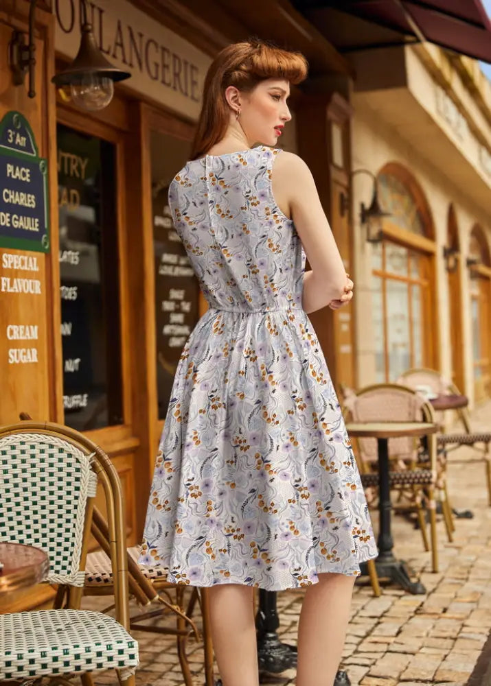 A woman wearing a pollinators vintage blue floral cotton a-line dress with pockets and a fitted waist
