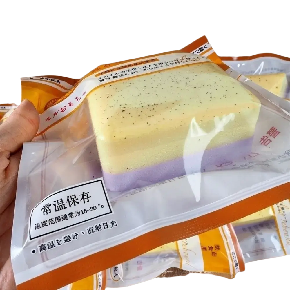 A rectangular layered soap bar with pale yellow and purple layers packaged in clear plastic with orange and white labeling containing polyester acrylic