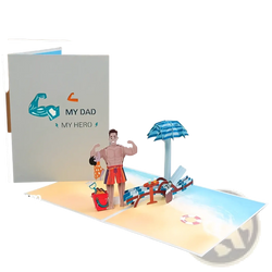 A handmade pop up fathers day card featuring a muscular man in red swim trunks on a beach with umbrella and chairs