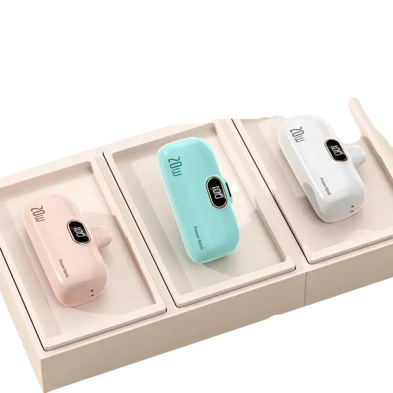 Three pastel-colored portable power bank chargers in pink, light blue, and white with built-in cables in a beige box