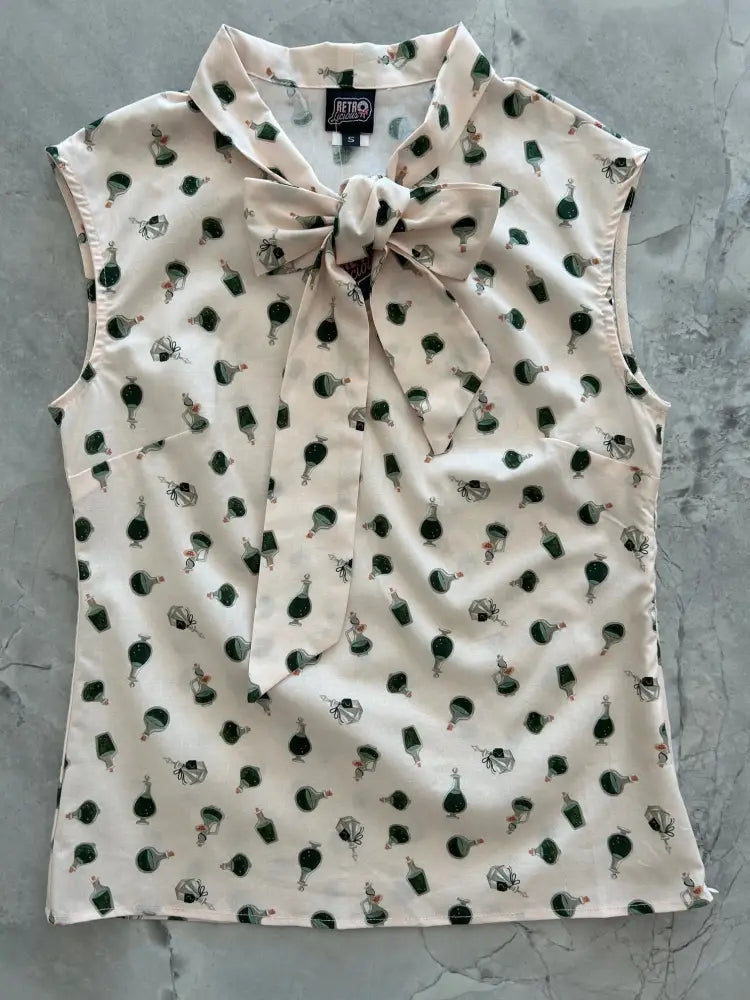 A cream sleeveless blouse with green and black vintage perfume bottle print and matching bow at the collar with side zipper