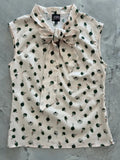 A cream sleeveless blouse with green and black vintage perfume bottle print and matching bow at the collar with side zipper