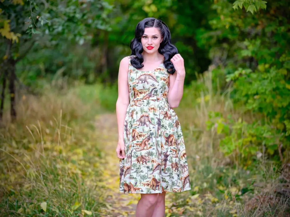 A vintage prehistoric dinosaur print sleeveless cotton A-line dress in earthy tones on a light green background