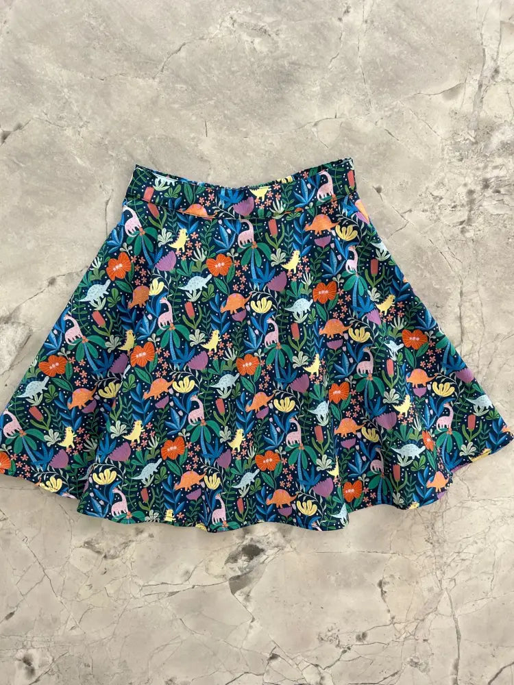 A vibrant prehistoric dinosaur floral print skater skirt with colorful patterns on a dark teal background