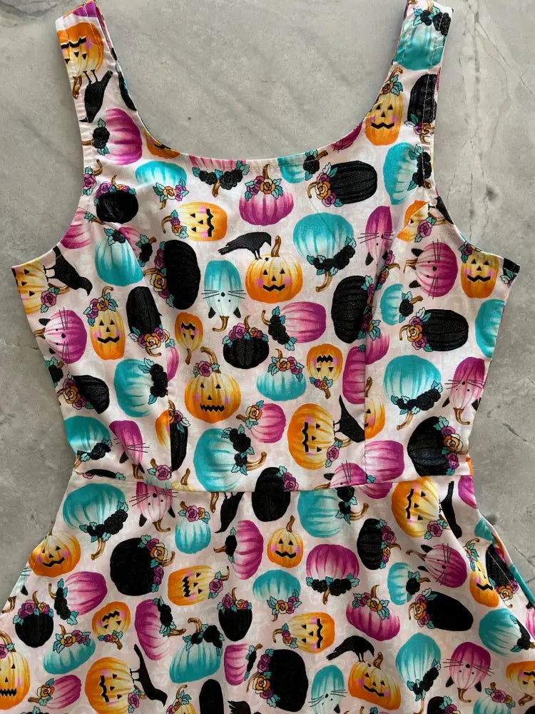 A vibrant Halloween-themed sleeveless skater dress with colorful pumpkins black cats and jack-o-lanterns on light fabric