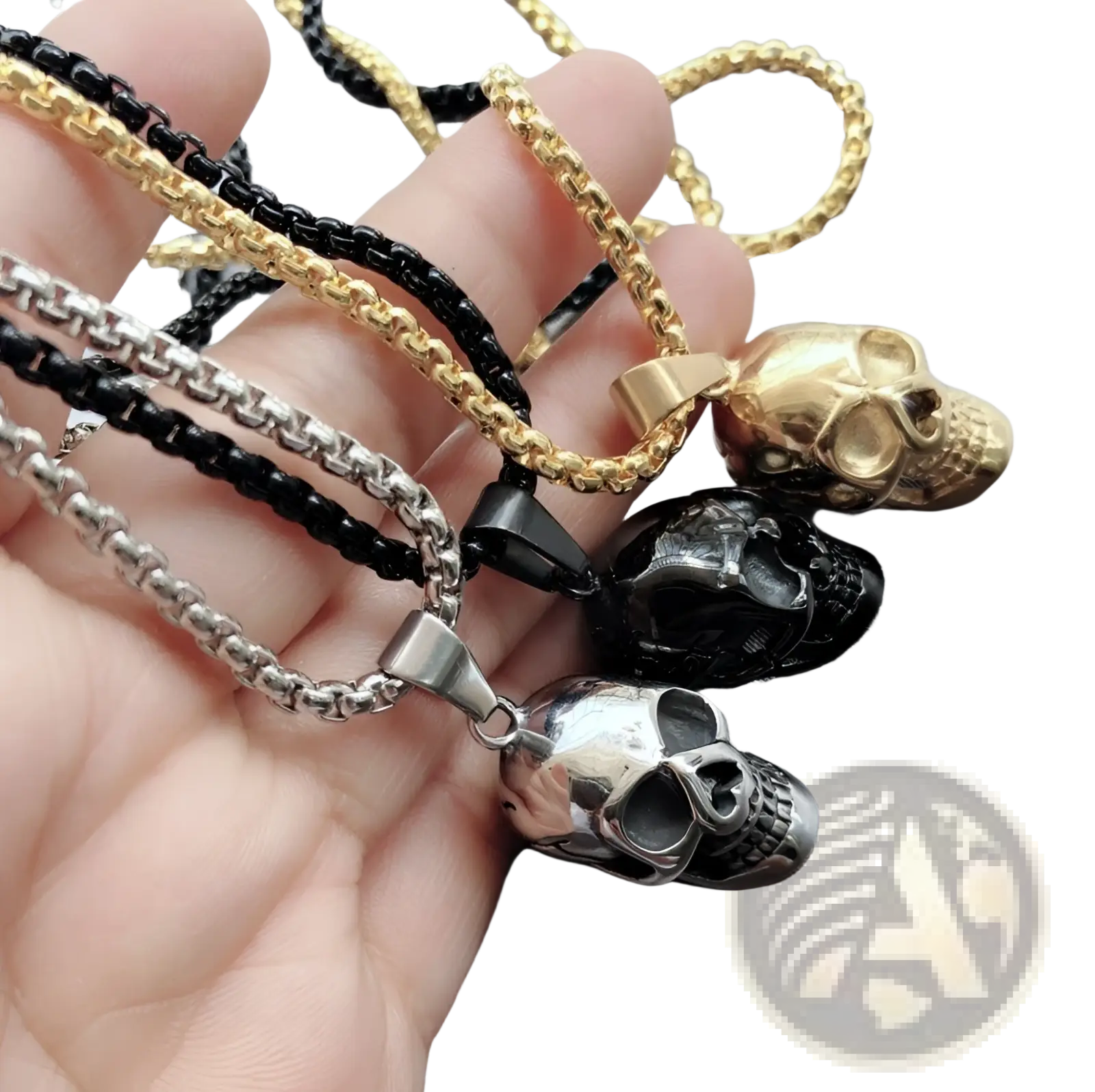 A hand holds three punk skull pendant titanium steel necklaces in gold, blackened steel, and polished silver finishes