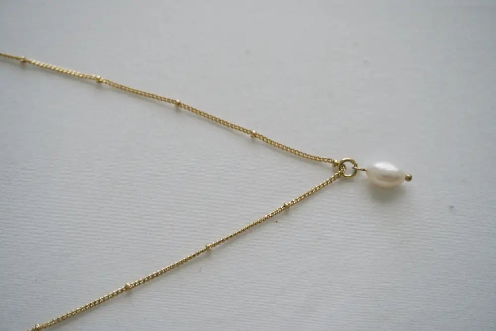 A delicate gold chain necklace with a single white pearl pendant from the pure pearl and gold bead layered set