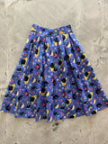 A vibrant blue pleated cotton skirt with pockets featuring black cats colorful hearts and yellow moons pattern