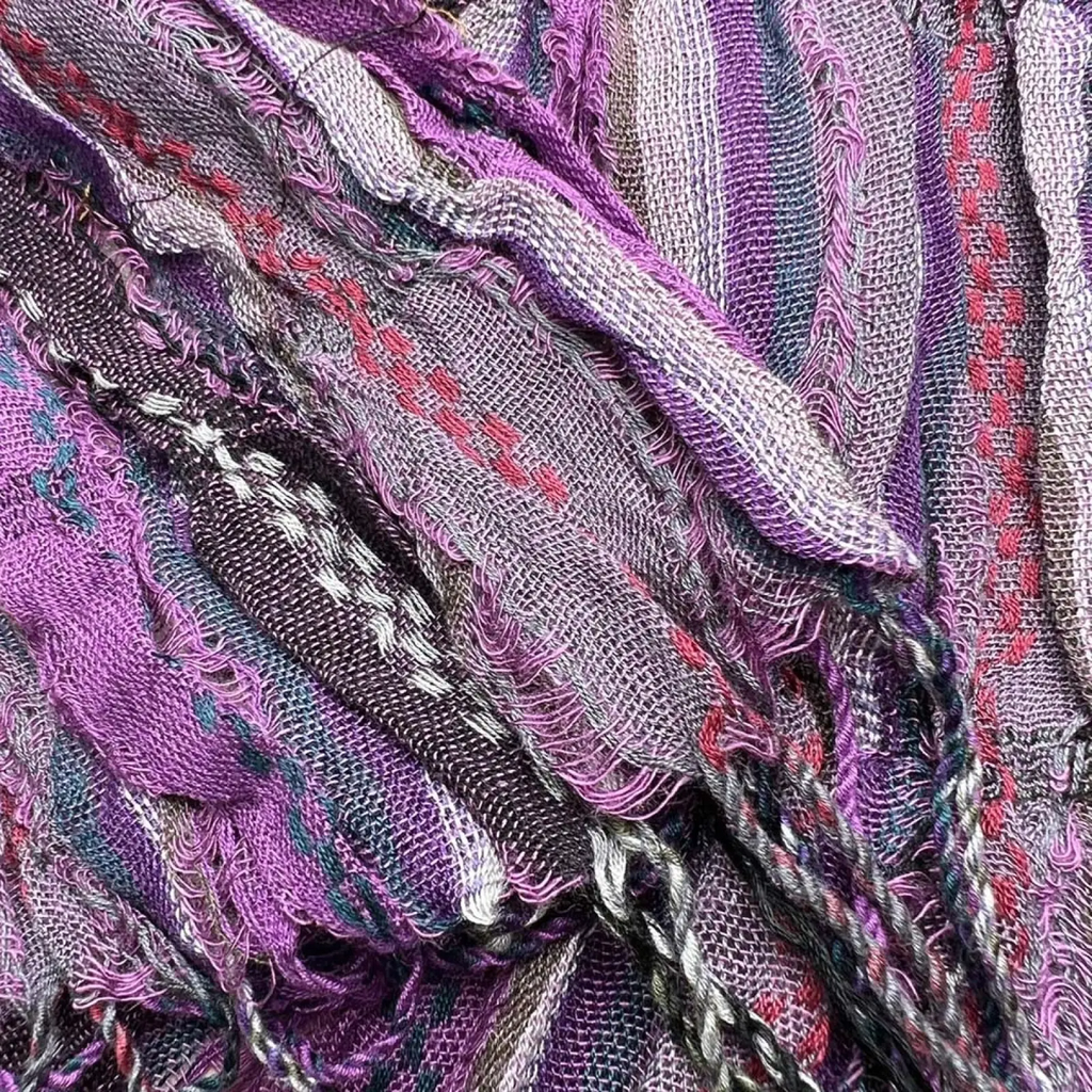 A textured purple jacquard crinkle scarf with woven patterns and frayed edges in shades of purple gray pink and black