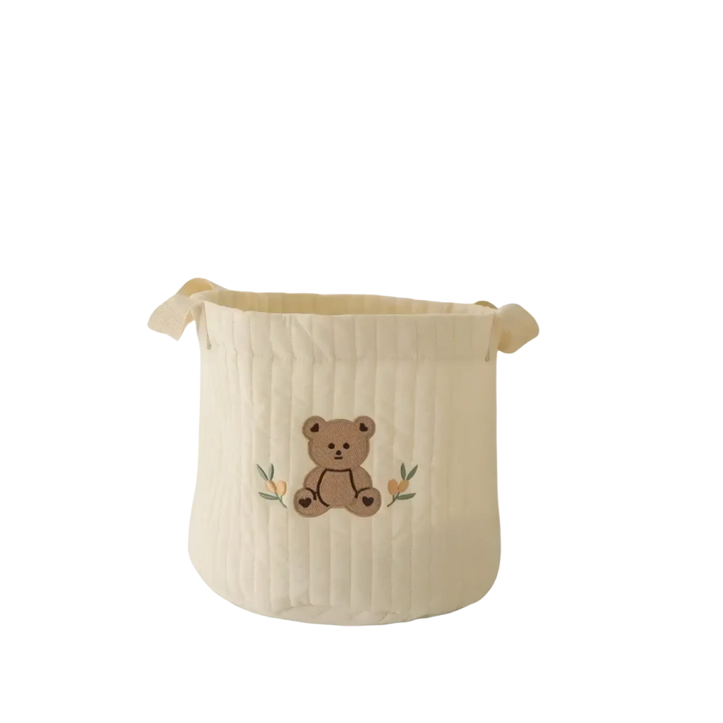 Cream-colored quilted fabric baby diaper storage basket organizer with embroidered brown teddy bear and green leaves