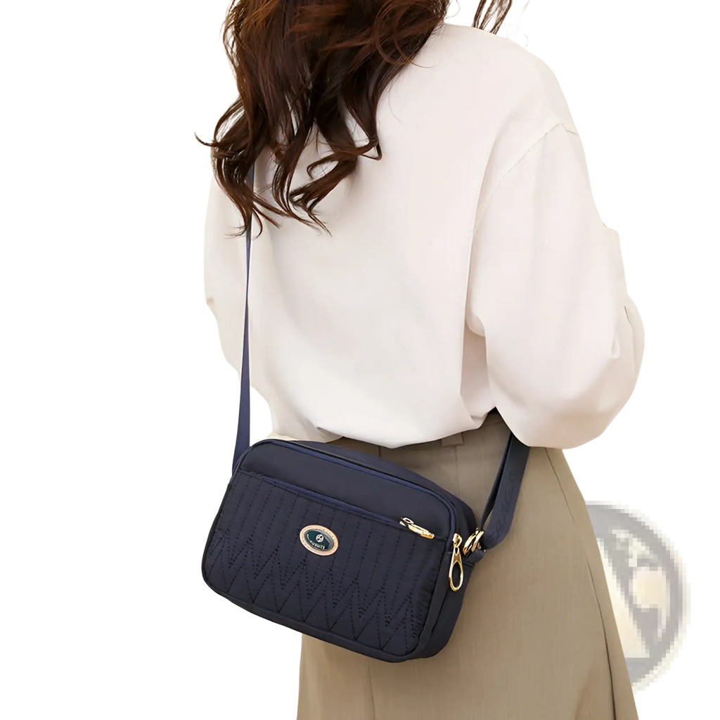 Navy blue quilted crossbody bag with gold hardware and circular logo plaque perfect for stylish daily use