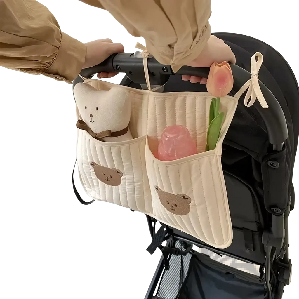 Cream-colored quilted stroller organizer bag with embroidered bear faces and attached plush teddy bear for storage