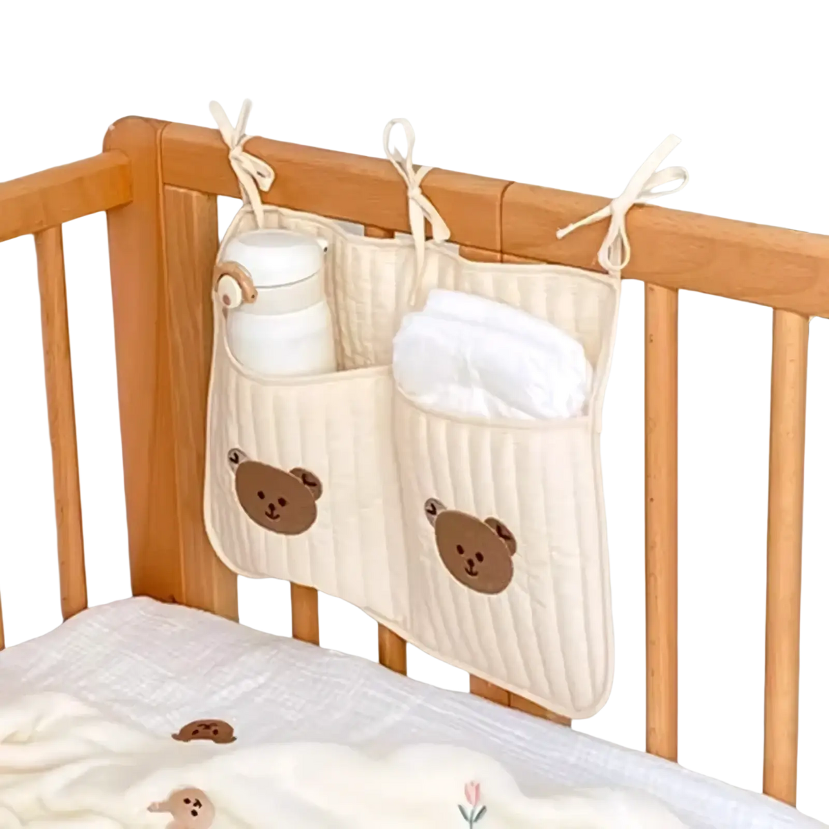 Cream-colored quilted stroller organizer bag with bear embroidery and three tied ribbon loops for hanging on crib sides