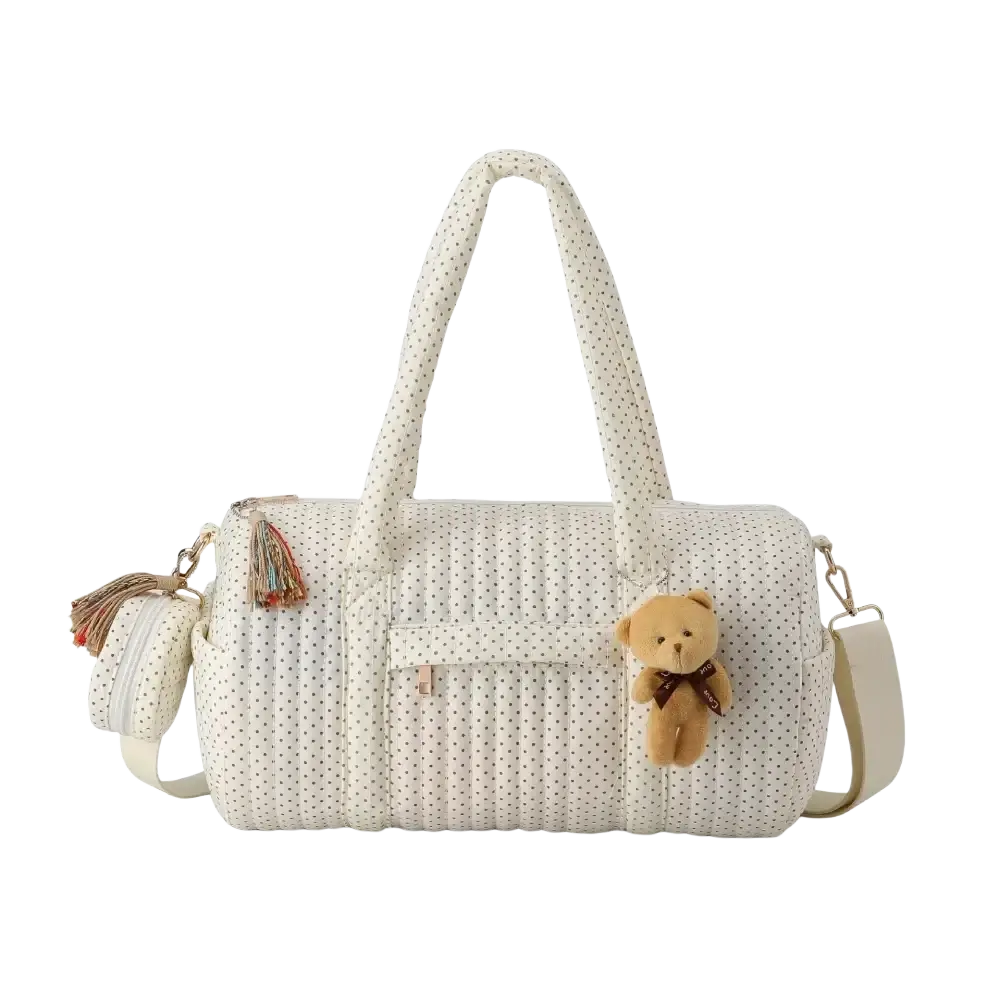Cream-colored quilted stroller organizer bag with black polka dots featuring plush teddy bear charm and tassel accents