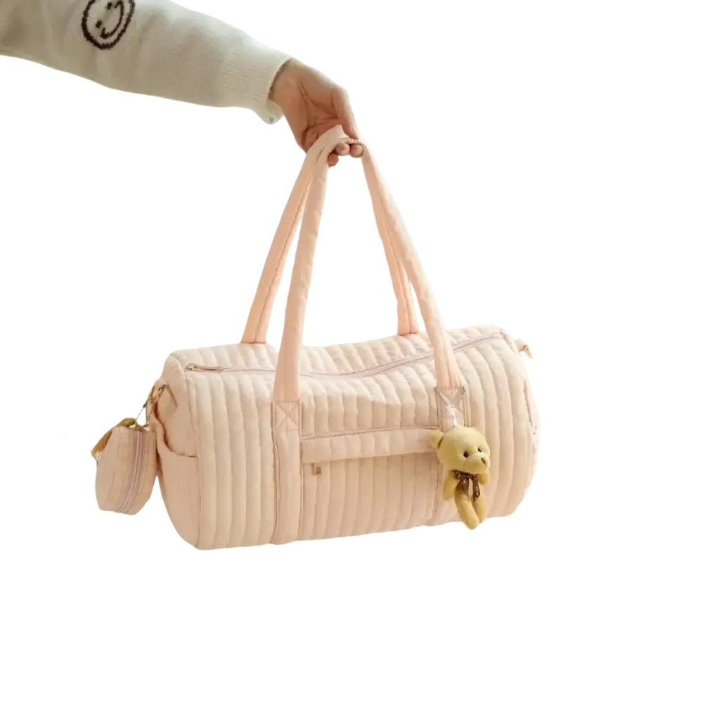 A soft pink quilted stroller organizer bag with long handles and a small teddy bear charm on the side