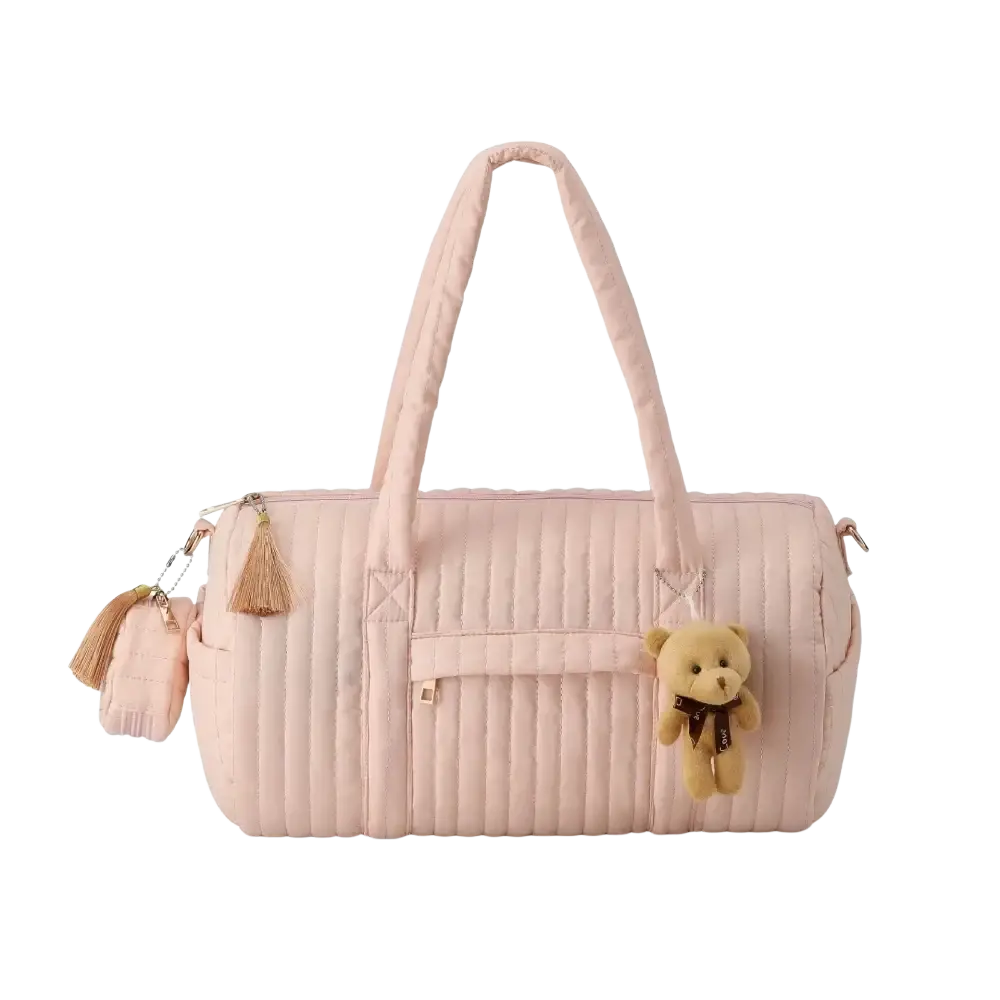 A soft pink quilted stroller organizer bag with matching handles decorative tassels and a small teddy bear charm