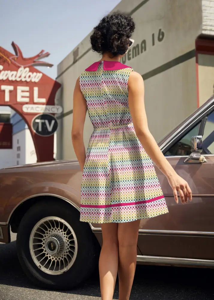A sleeveless knee-length cotton rainbow drop retro 60s dress with pastel stripes, polka dots, and pink peter pan collar