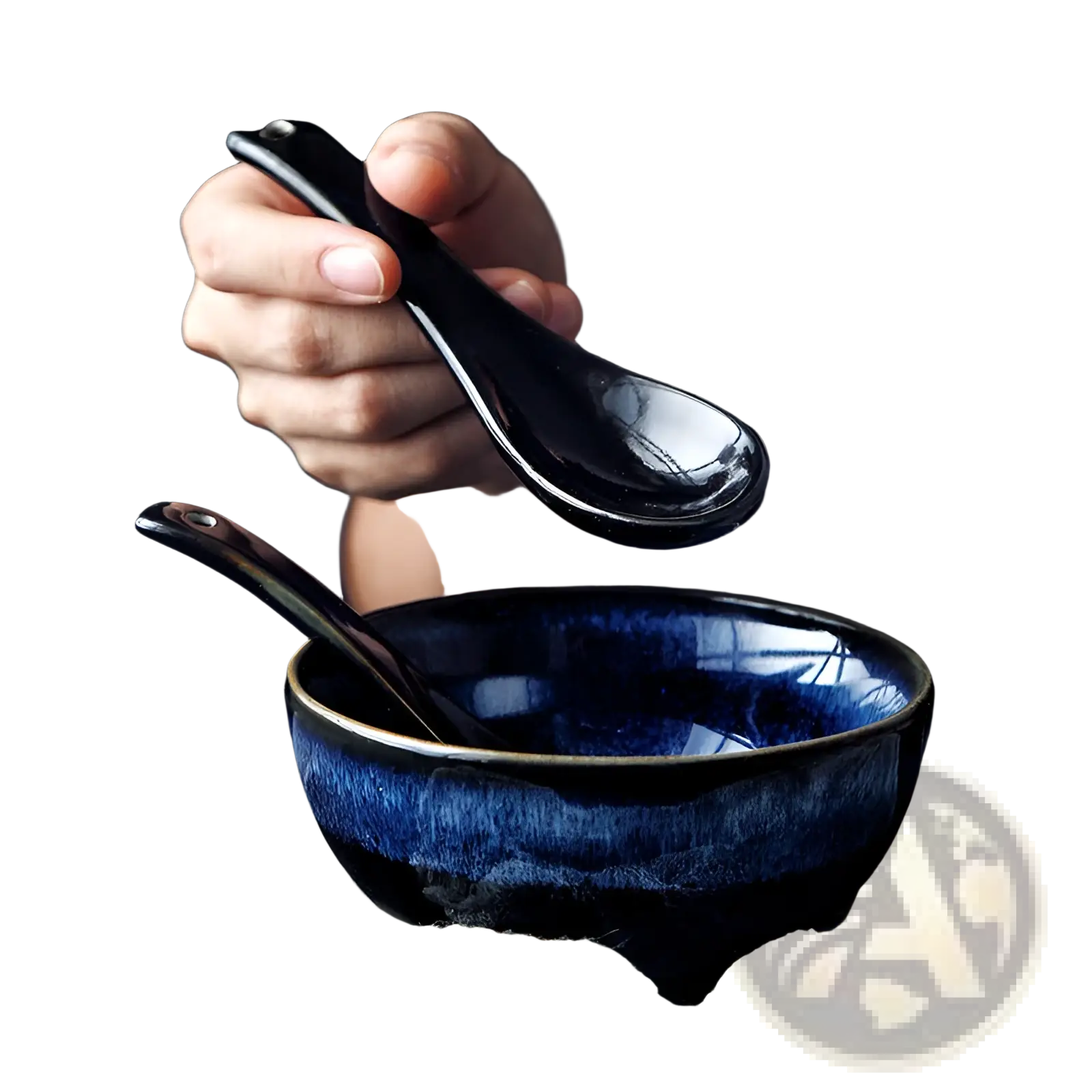 A glossy black ceramic spoon held above a deep blue 8.5 inch cat eye ceramic ramen bowl