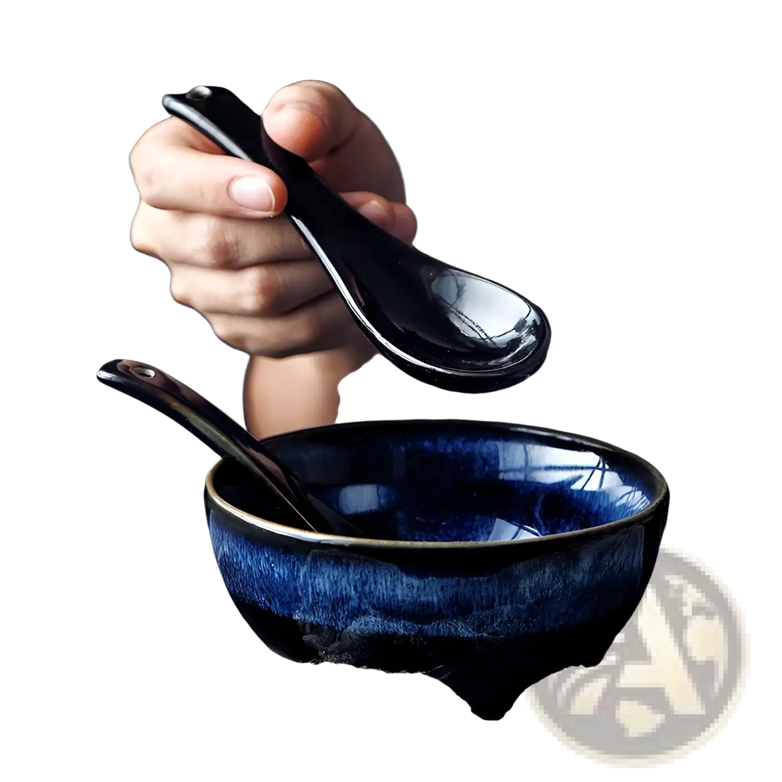A glossy black ceramic spoon held above a deep blue ramen bowl ceramic 8.5 inch cat eye noodle bowl
