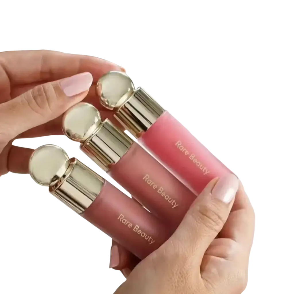 Three pink rare beauty soft pinch liquid blush glosses with gold spherical caps held in a hand