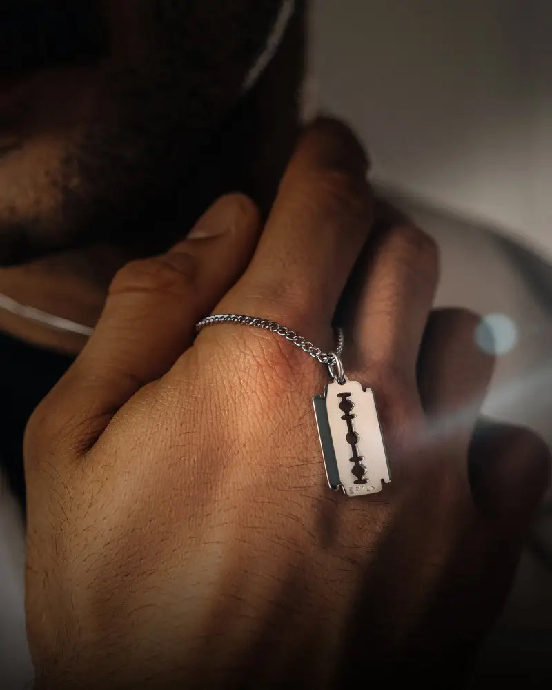 Silver razor blade pendant on a stainless steel curb chain necklace featuring a fine silver finish and durable design
