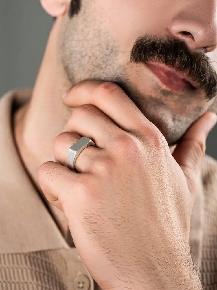A sleek silver-toned rectangular oxidized 316l stainless steel signet ring with a modern minimalist design worn on a man’s finger
