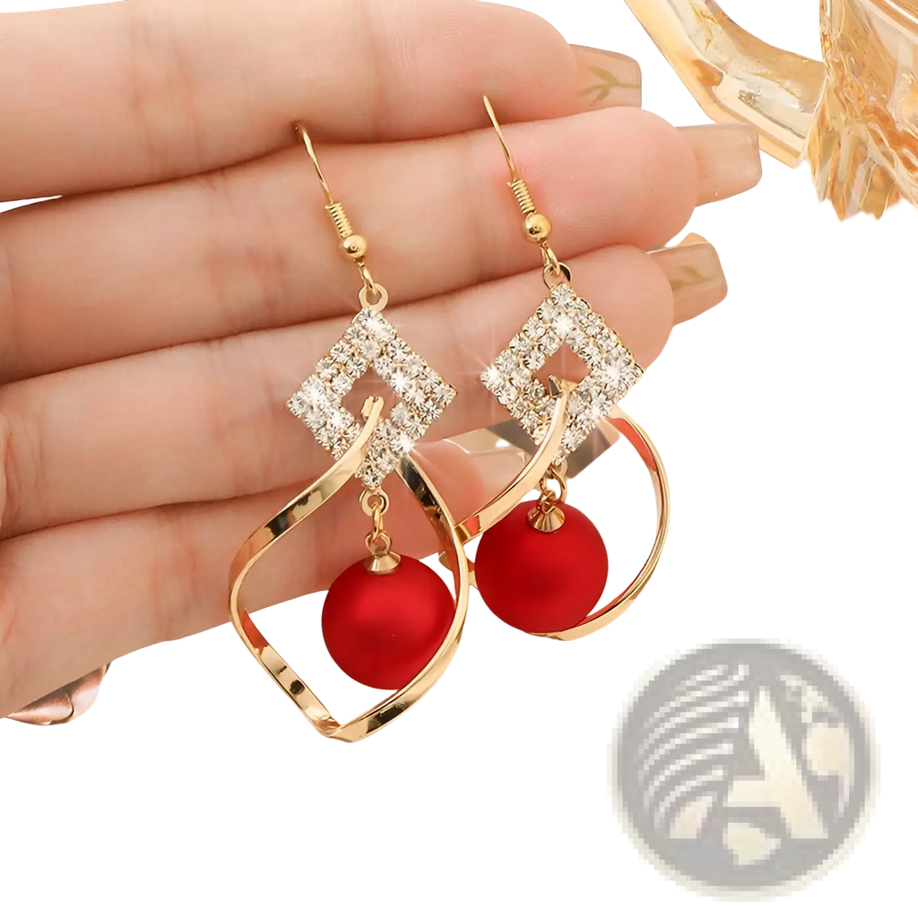 Gold dangle earrings with diamond-encrusted square tops and vibrant red bead pendants in a geometric design
