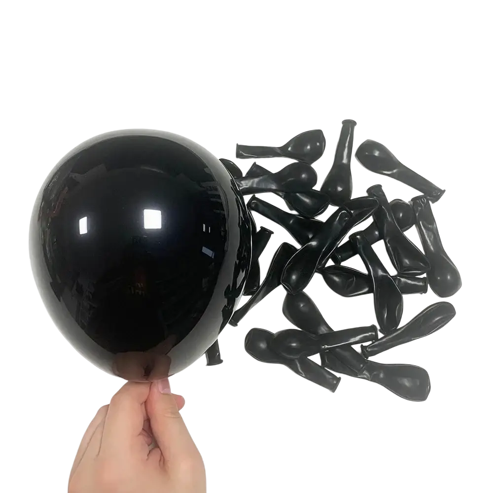 A hand holding a glossy black latex balloon with deflated black balloons for red black balloon garland arch kit