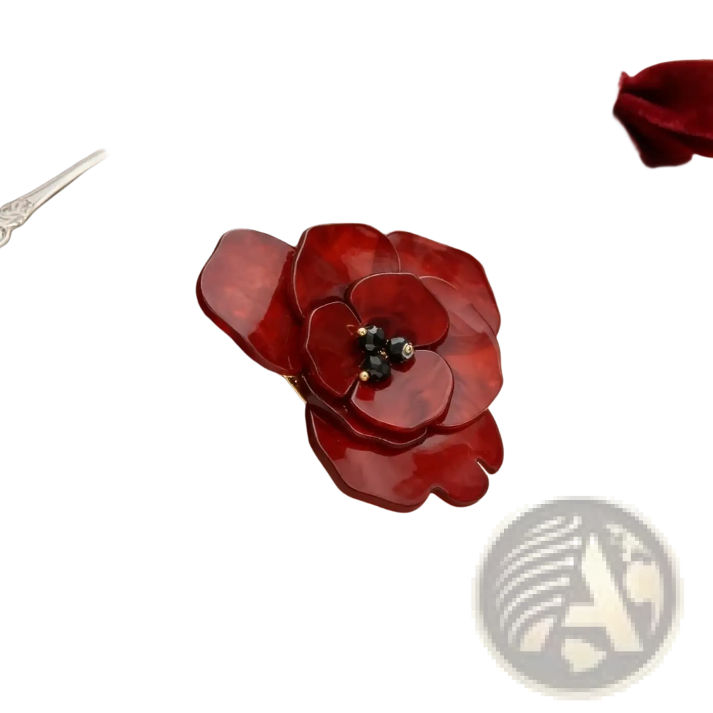 A glossy crimson enamel poppy pin shaped like a flower with a central cluster of black and gold beads
