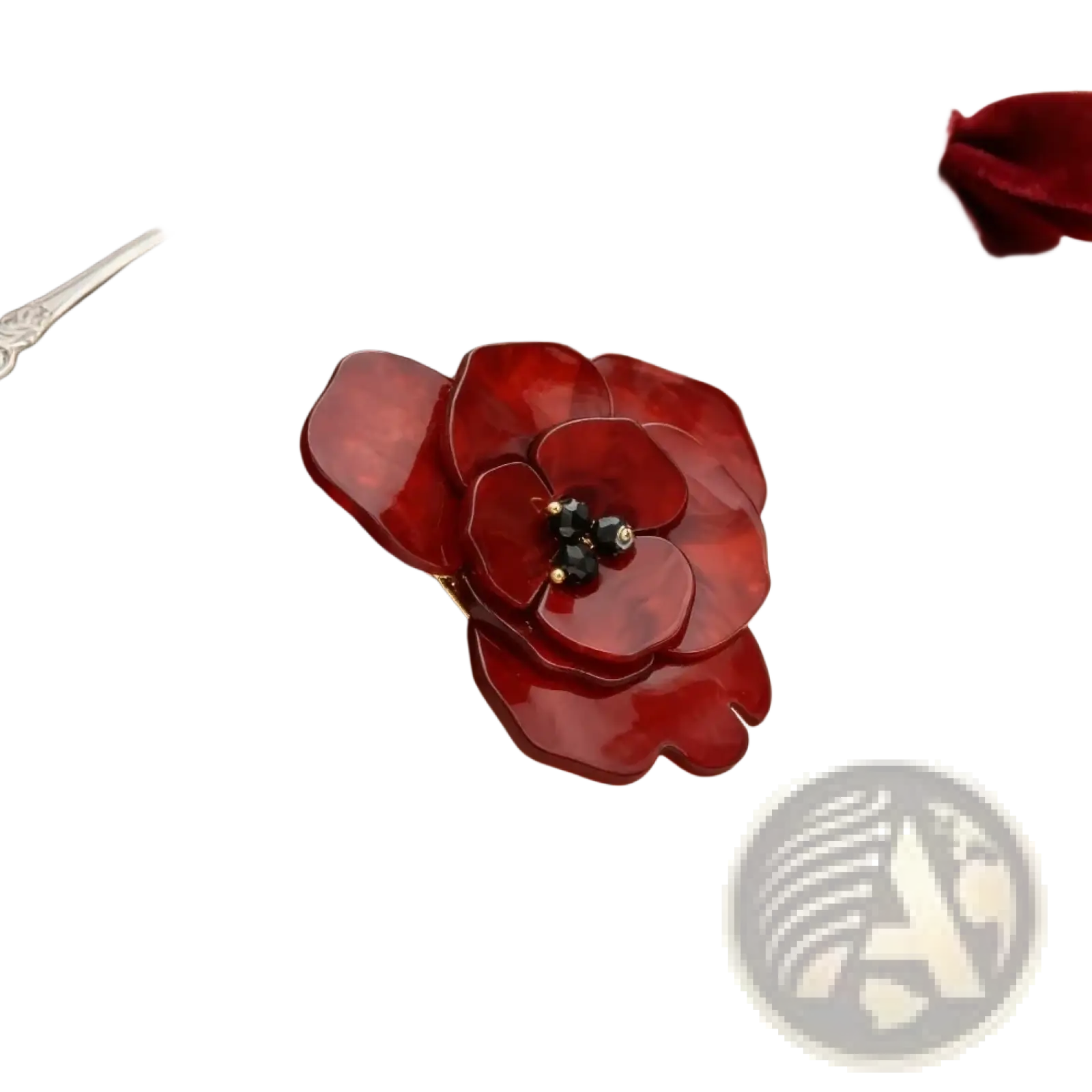 A glossy crimson enamel poppy pin shaped like a flower with a central cluster of black and gold beads