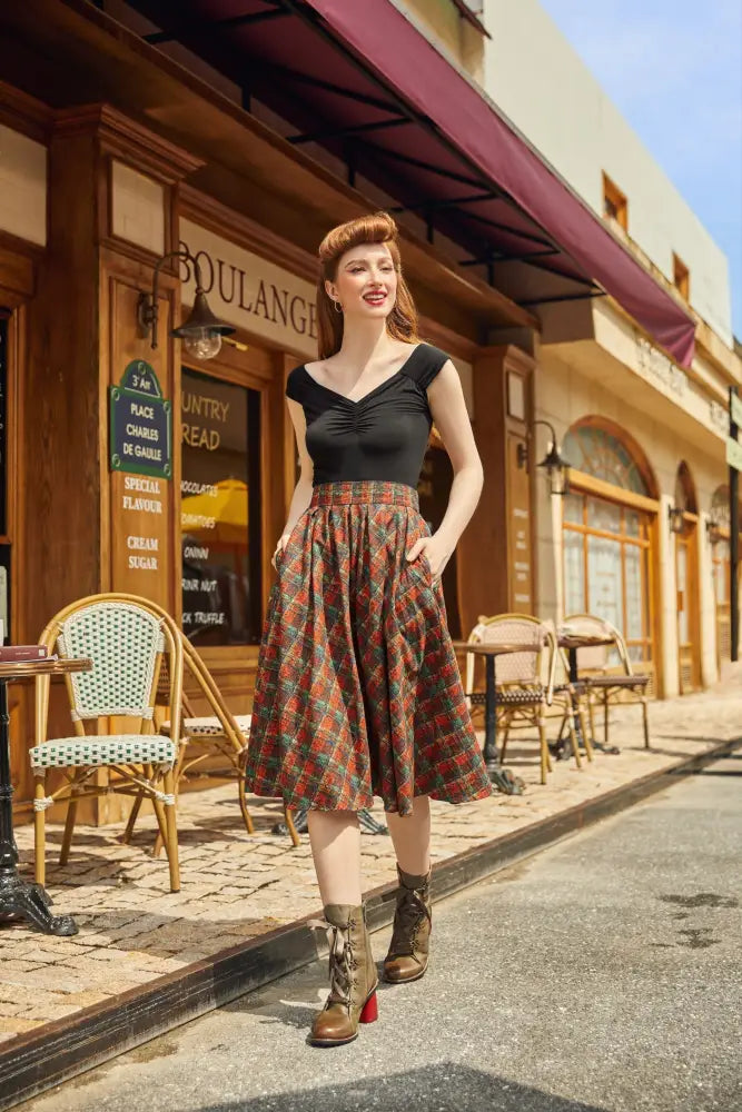 A woman wearing a holiday plaid Doris high waisted cotton flare skirt with pockets in red and green paired with a black sleeveless top
