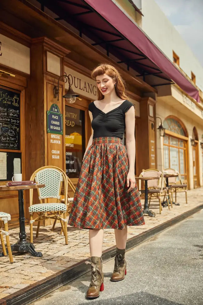 A woman wears a holiday plaid Doris high waisted cotton flare skirt with pockets in red green and beige plaid