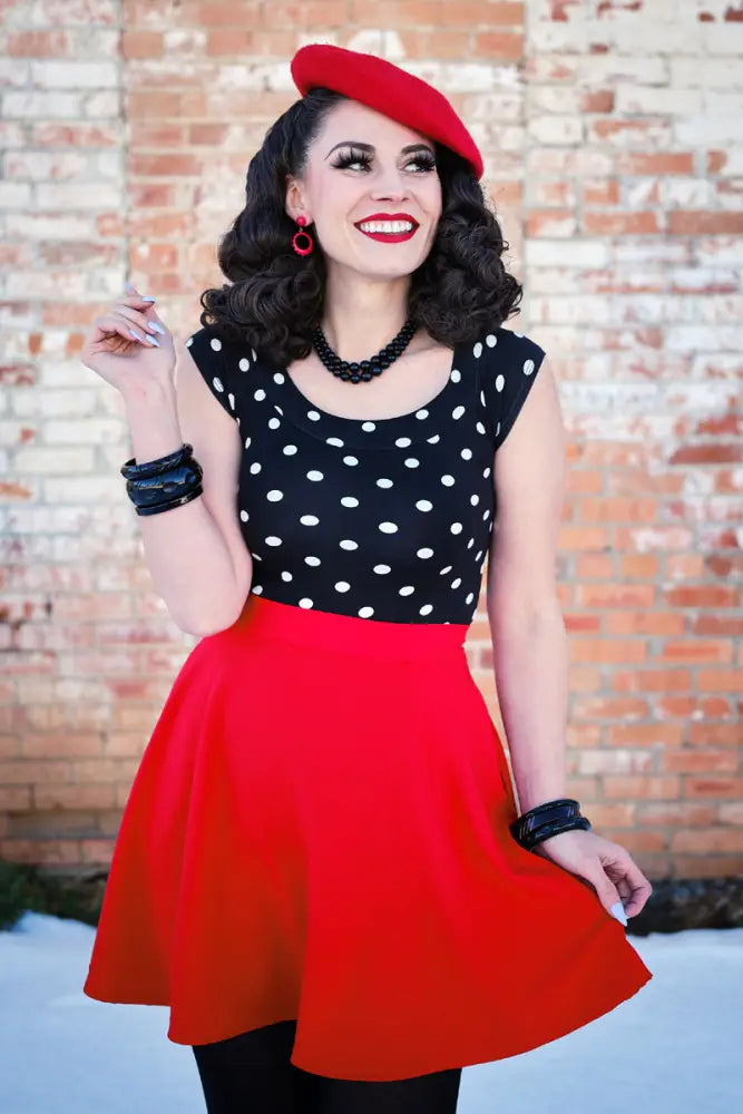 A woman wearing a vintage red skater skirt with pockets and elastic waist paired with a black and white polka dot top