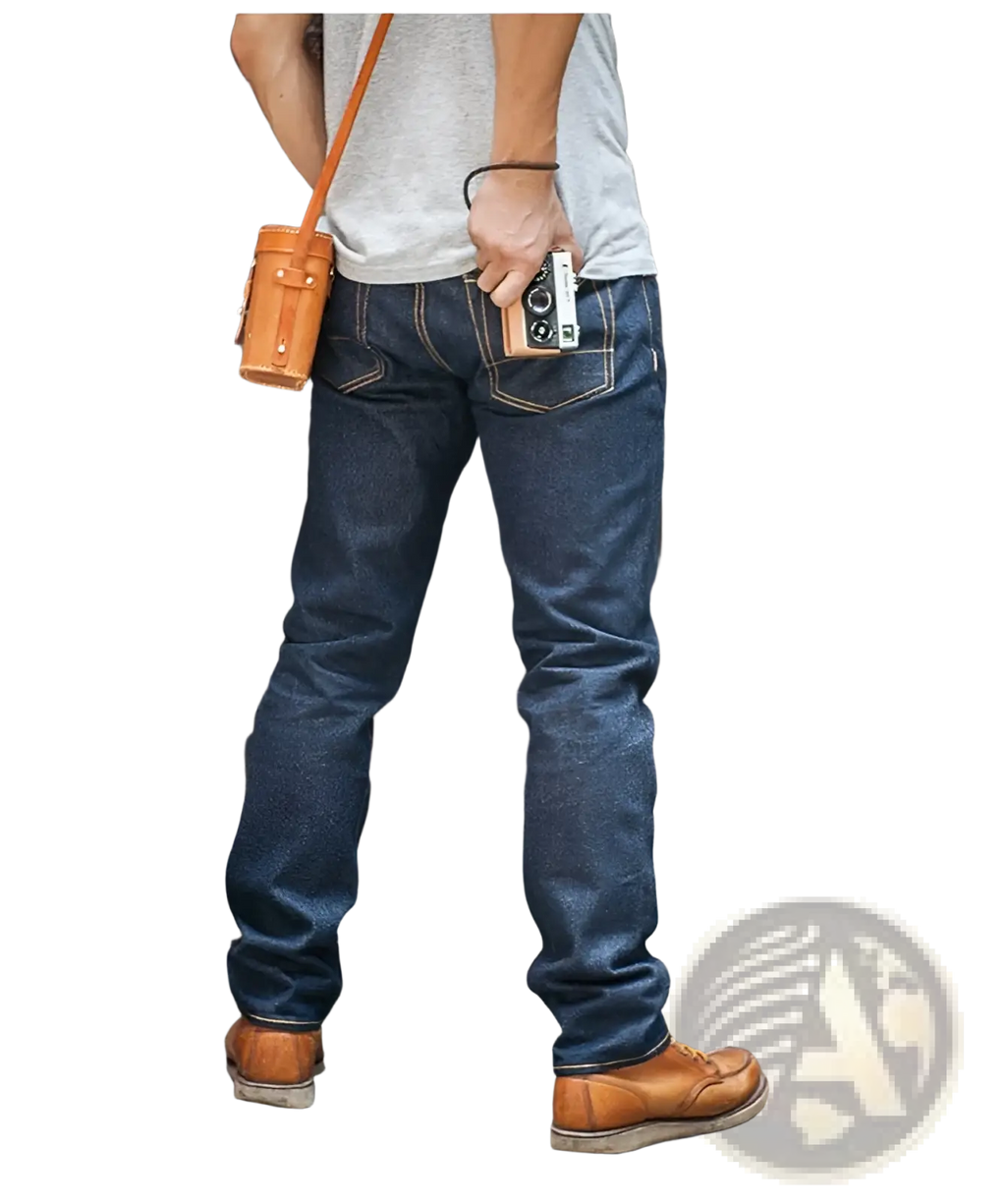 A tan leather camera pouch with sturdy strap and stitching worn over the shoulder paired with red tornado 16oz slim straight selvedge jeans