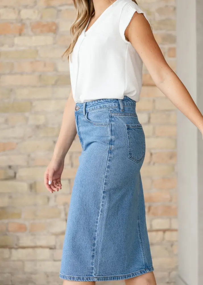 A mid-thigh length remi classic wash stretch denim midi skirt in medium-wash blue with button fly and two back pockets shown from the back