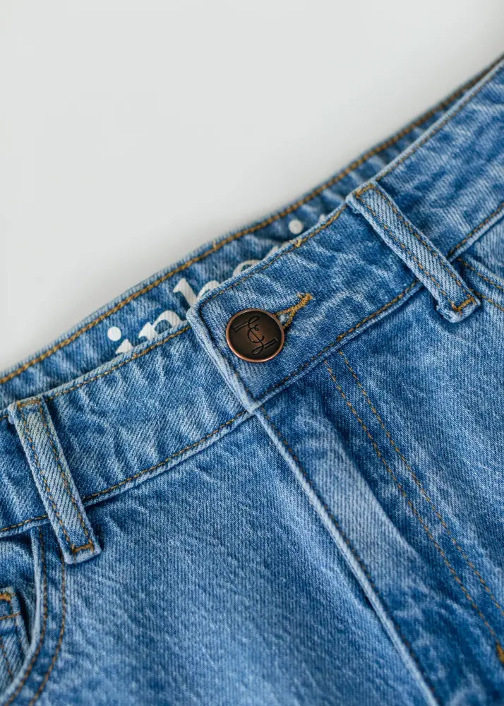 Remi classic wash stretch denim midi skirt in blue with a brown metal button featuring an engraved logo