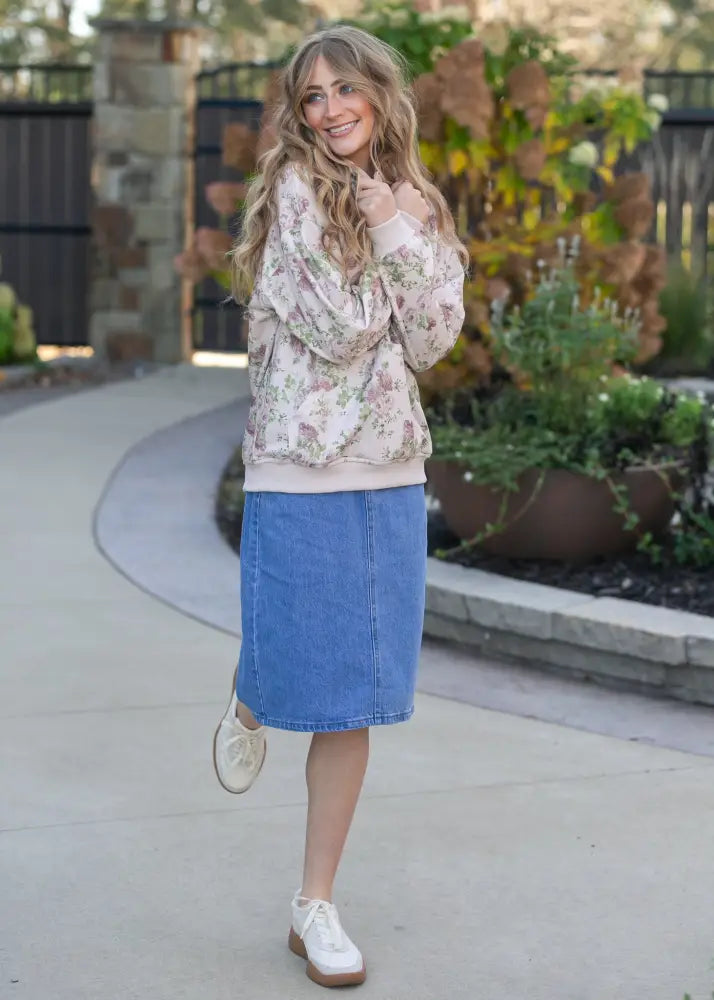 A woman wearing a remi classic wash stretch denim midi skirt with a floral patterned long sleeve top in pastel tones