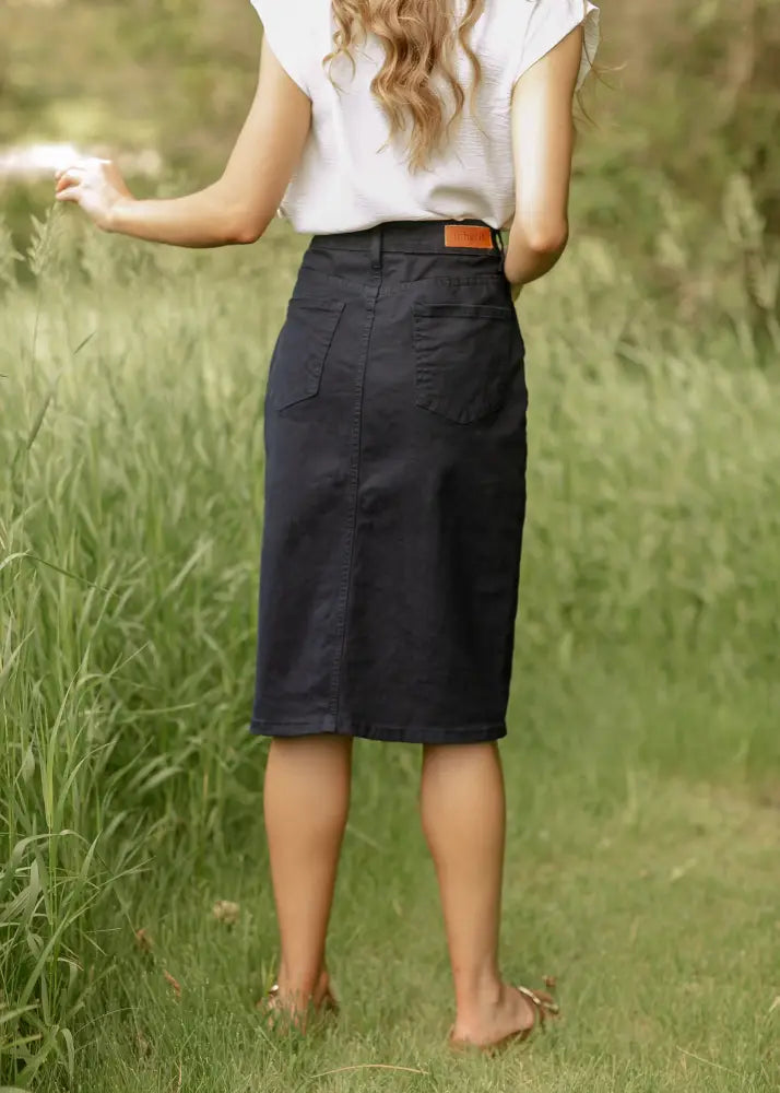 Back side view of remi navy high waisted stretch denim midi pencil skirt with two pockets and orange leather belt loop