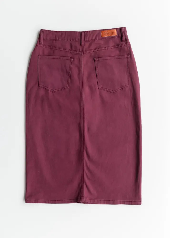 Back side of a remi orchid burgundy denim midi skirt featuring maroon fabric, two pockets, and a brown leather brand patch