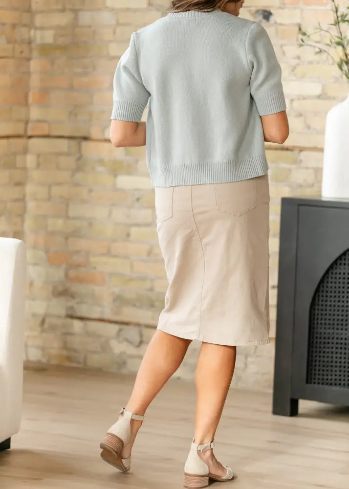 A woman wears a light blue knitted cardigan and a beige Remi Simply Taupe stretch denim pencil midi skirt