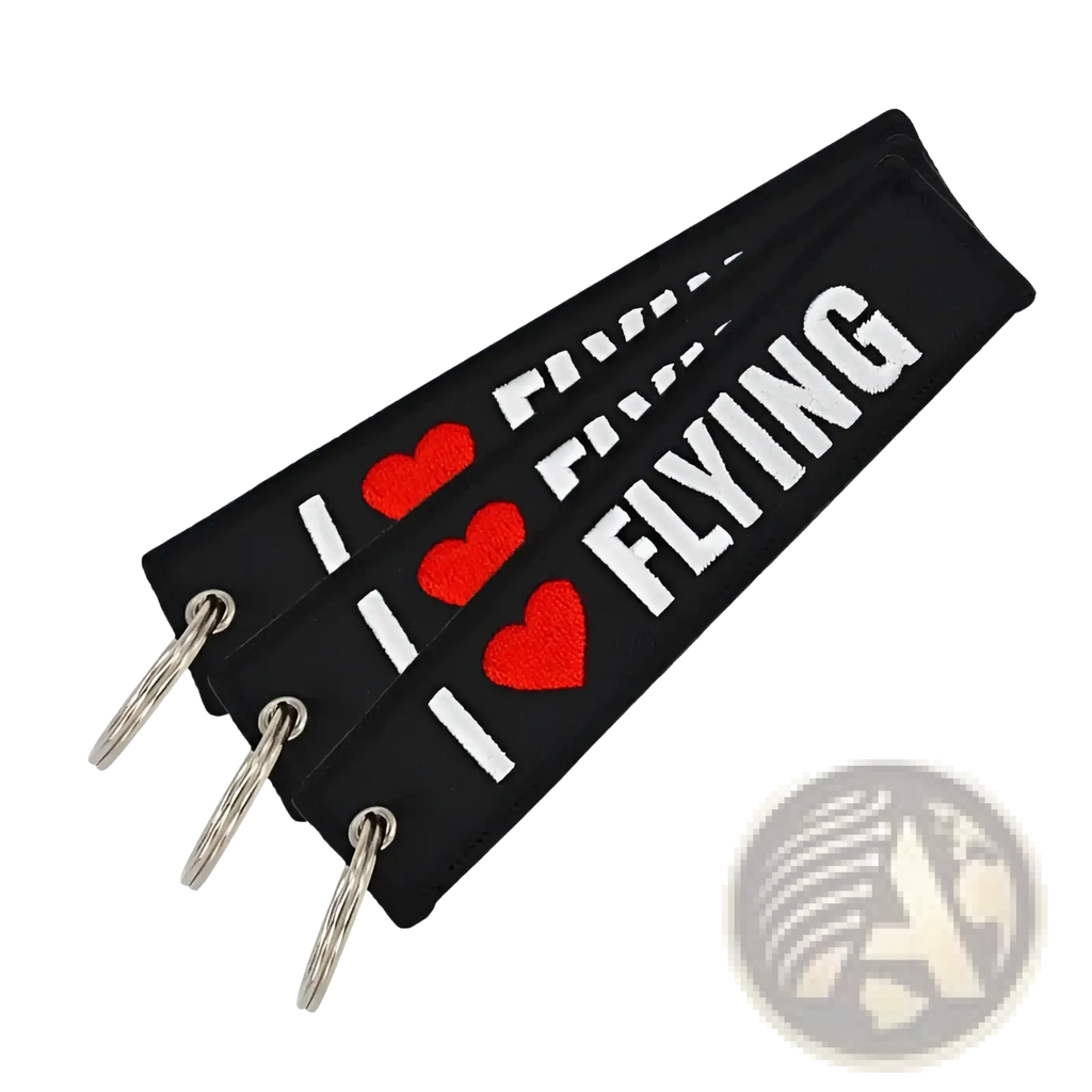 Black fabric Remove Before Flight keychain with embroidered red hearts and white i heart flying text