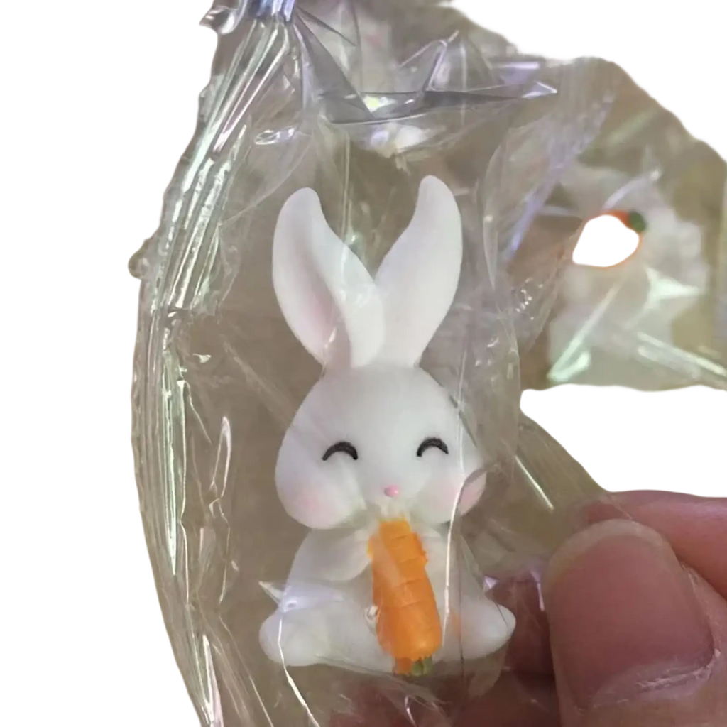 White resin bunny figurine with closed eyes and pink nose holding an orange carrot for Easter garden and cake decor