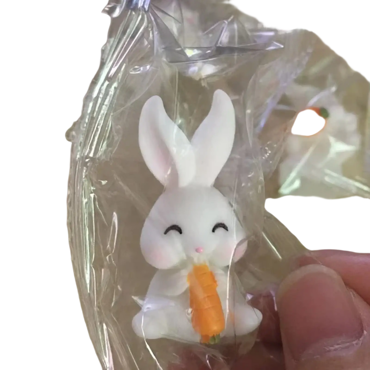 White resin bunny figurine with closed eyes and pink nose holding an orange carrot for Easter garden and cake decor