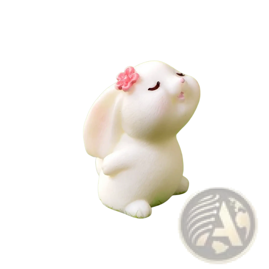 A white resin bunny figurine with closed eyes and a pink flower on its head sitting on green moss for Easter decor