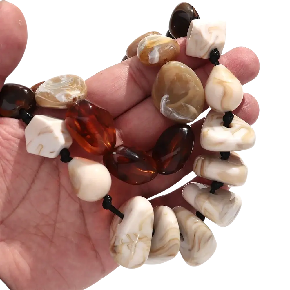 A hand holds a resin geometric marbled beaded choker necklace with amber and cream stones on black cord