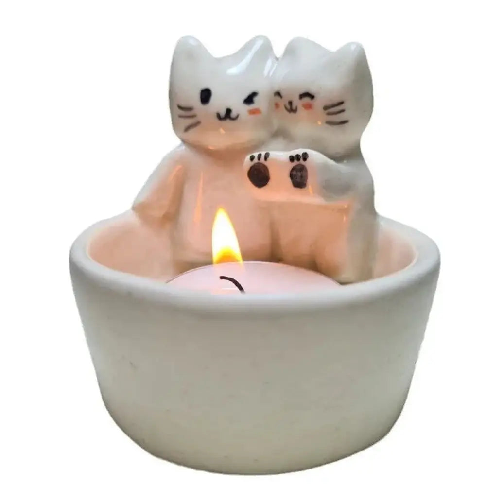 White ceramic candle holder featuring two stylized cuddling kittens with black and orange facial details
