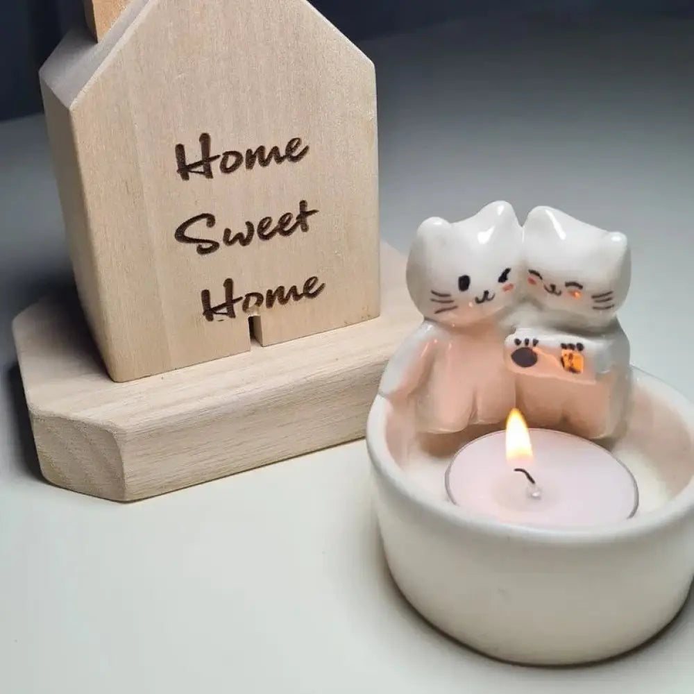 Handcrafted cuddling kittens ceramic candle holder with two white cat figurines holding a camera on a lit pink tea light